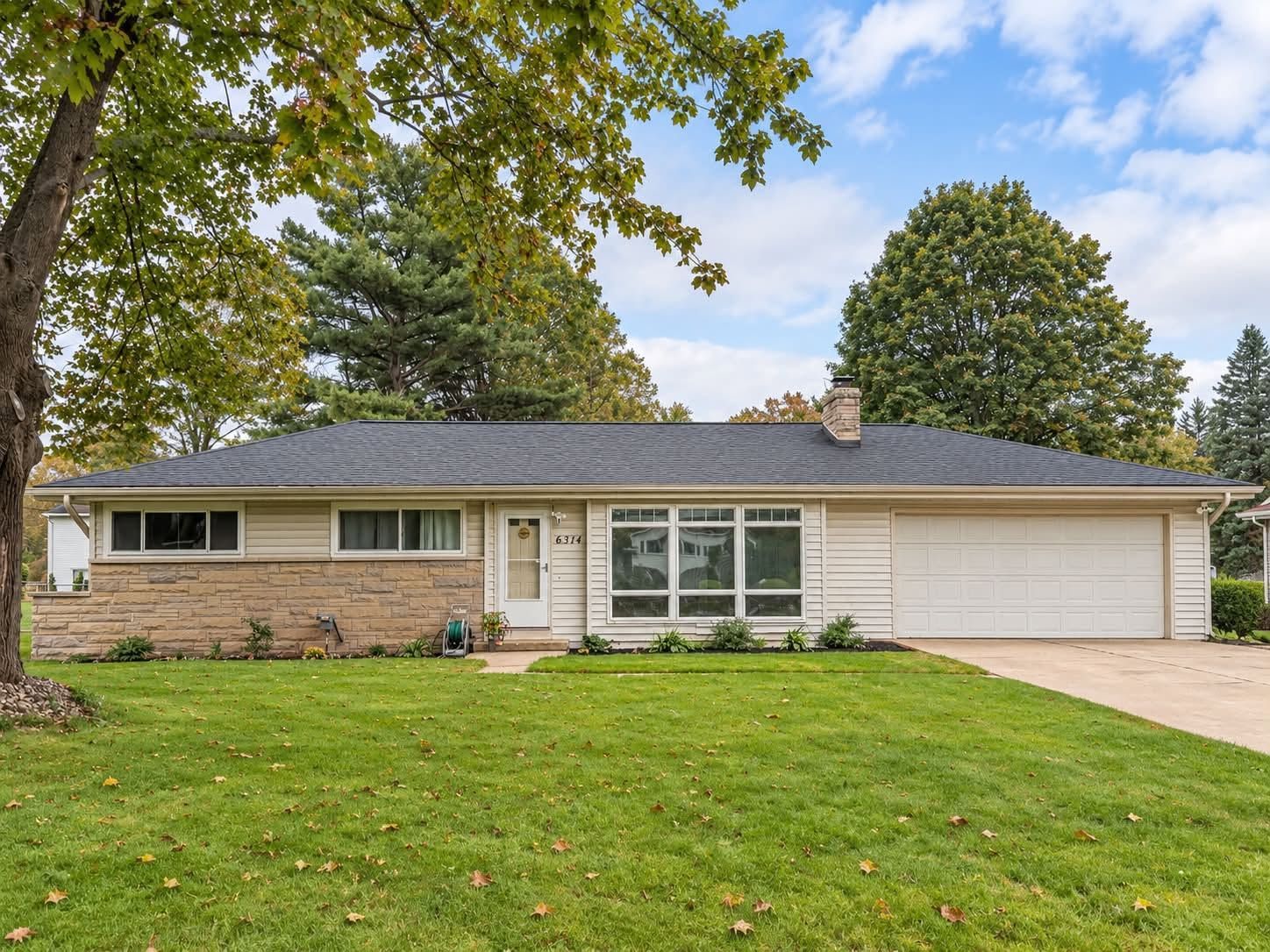 Single-story suburban house with brick and beige siding, front lawn, trees, and attached garage