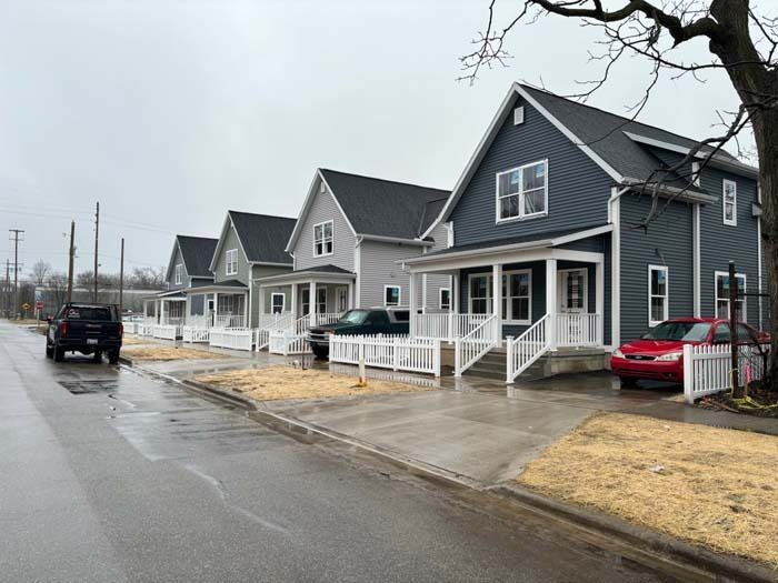 Row of gray suburban houses on a rainy street, with parked cars and white porches