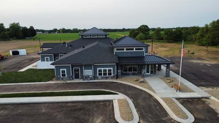 Aerial view of a gray building with a circular driveway, parking lot, and landscaped grounds.