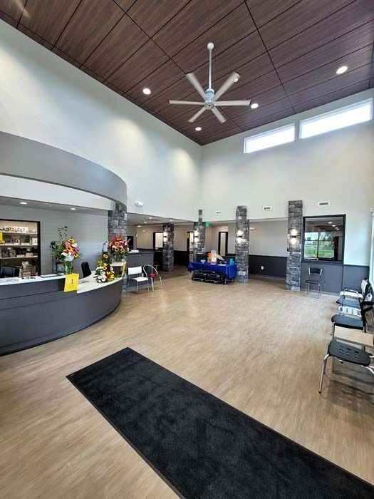 Modern lobby with curved reception desk, high wood ceiling, ceiling fan, seating, and glass entry doors