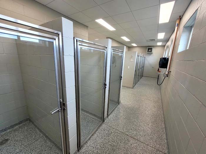 Public restroom with multiple shower stalls and tiled walls, viewed down a narrow corridor.