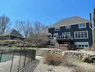 Backyard patio with deck and pool beside a large dark gray house under a blue sky