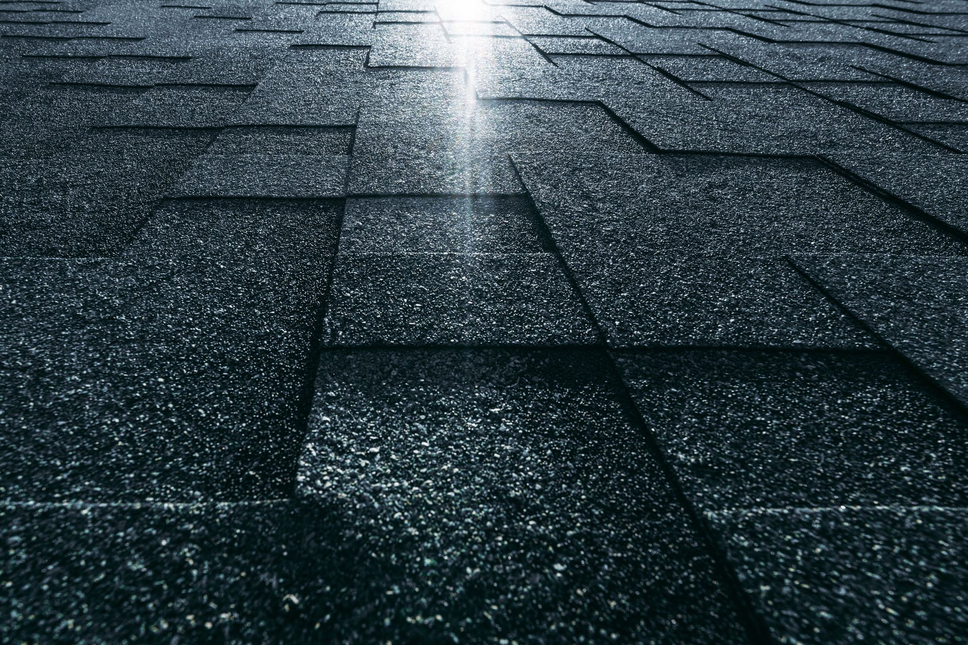 Close-up of dark roof shingles with wet sunlight reflecting down the center