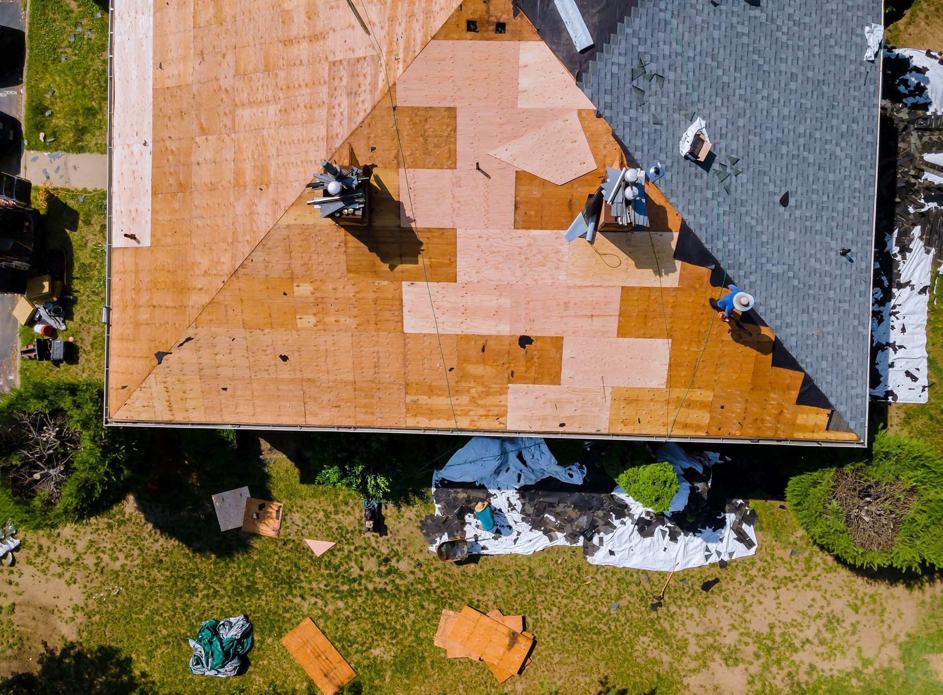 Aerial view of roofers working on a partially covered roof with orange underlayment and scattered materials below