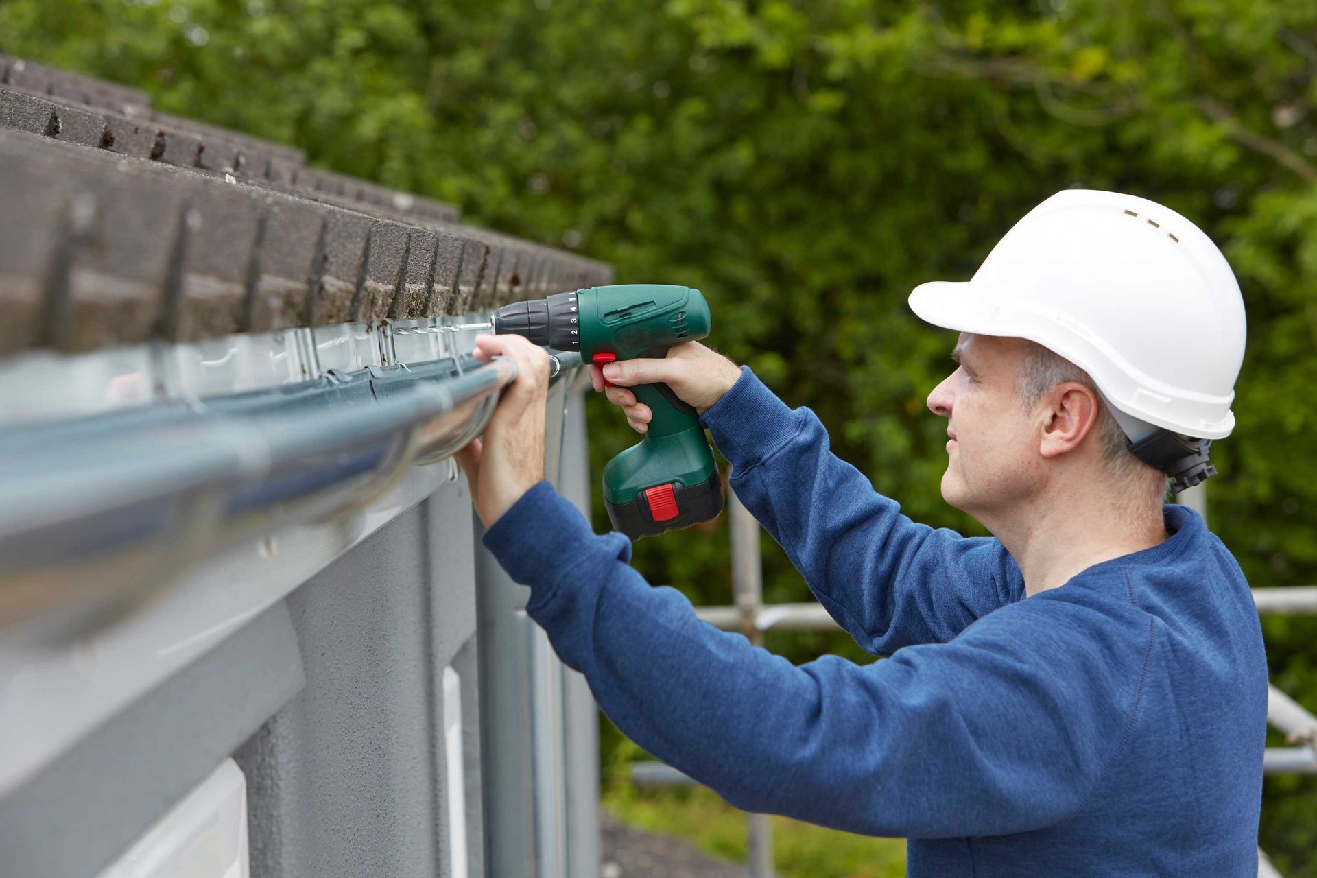 A technician installing residential gutters with a power drill. A technician installing residential gutters with a power drill.