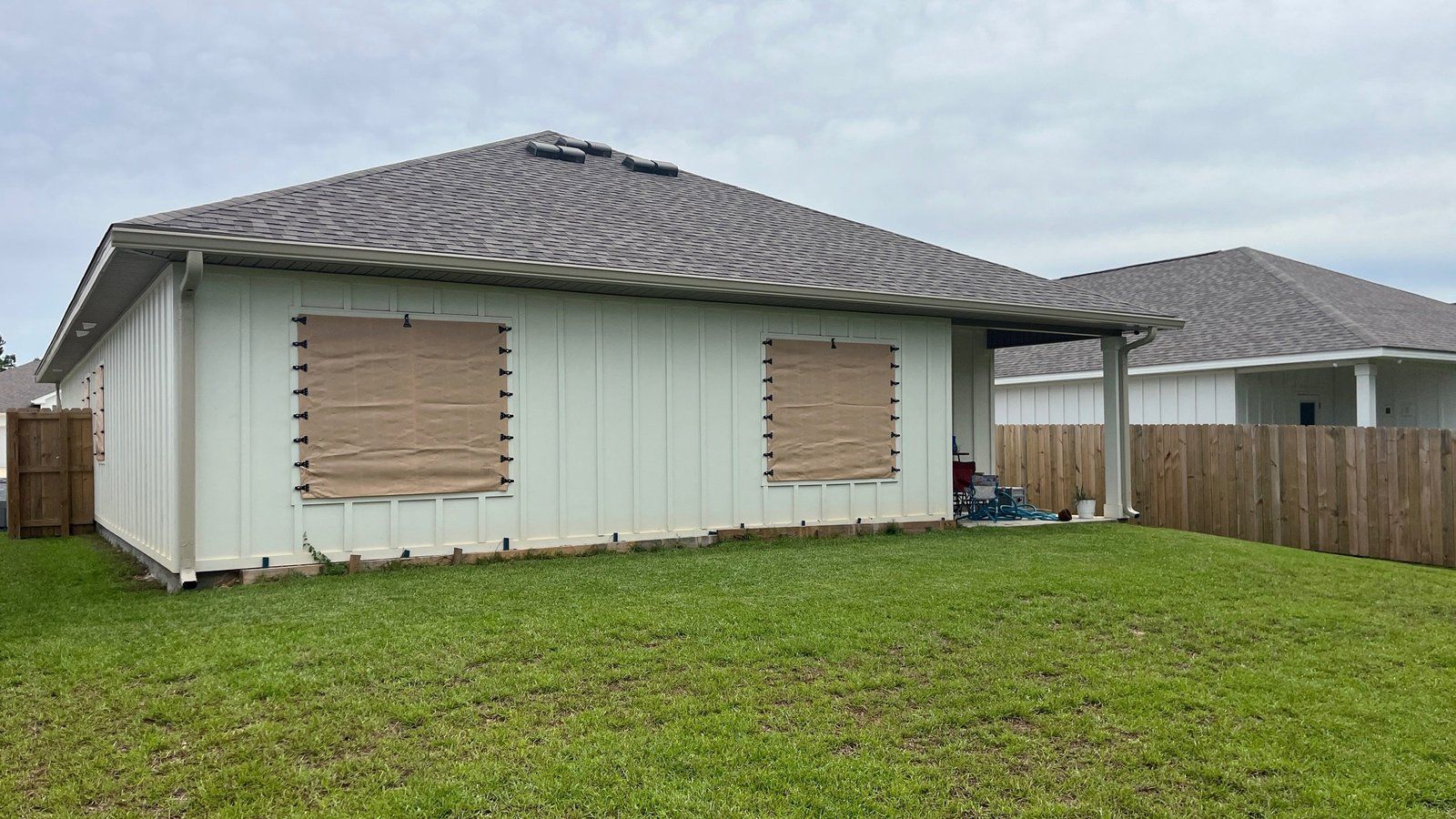 Back of a home in Mobile, AL with gutters, downspouts and plywood over the windows
