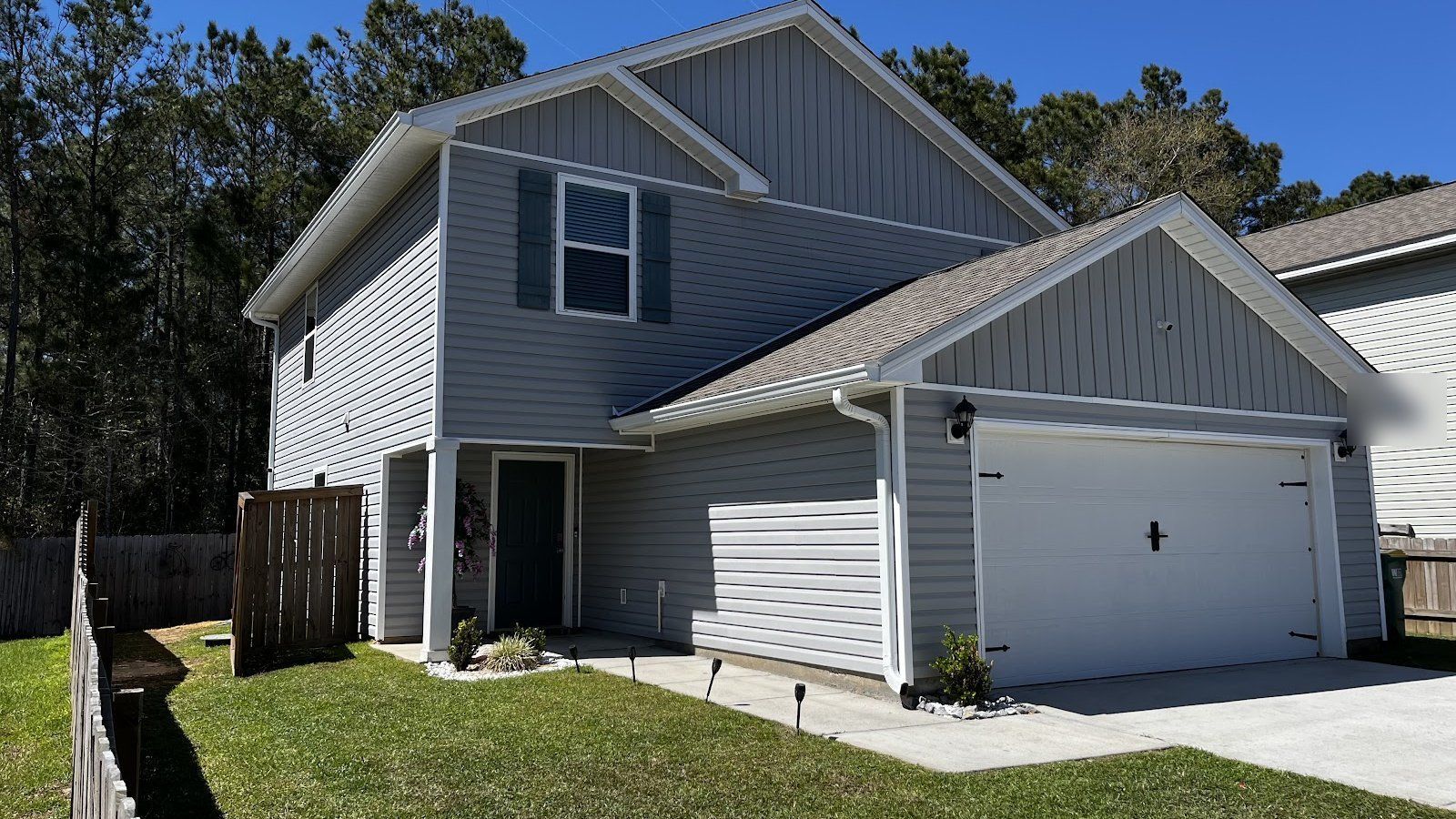 Gray two-story home with white gutters and downspouts and pine trees behind it