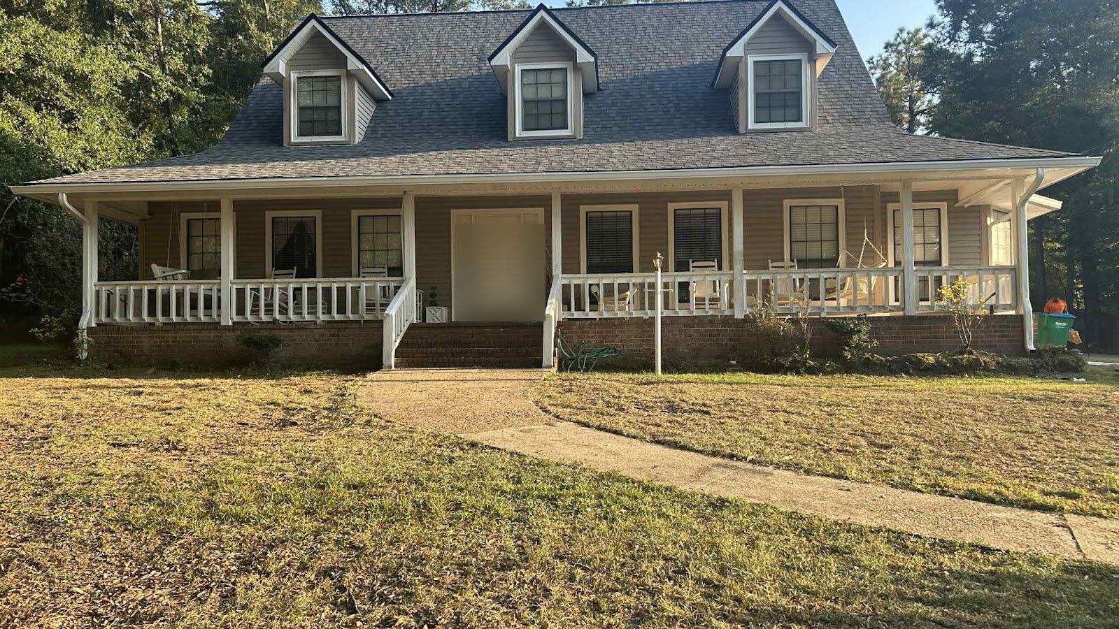 Two-story home with dormers, a long covered front porch and white seamless gutters and downspouts, with pine trees around the lot
