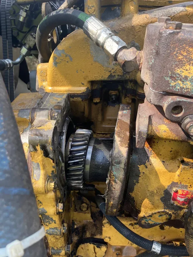 Close-up of a yellow engine with exposed gears, various hoses, and oil residue.