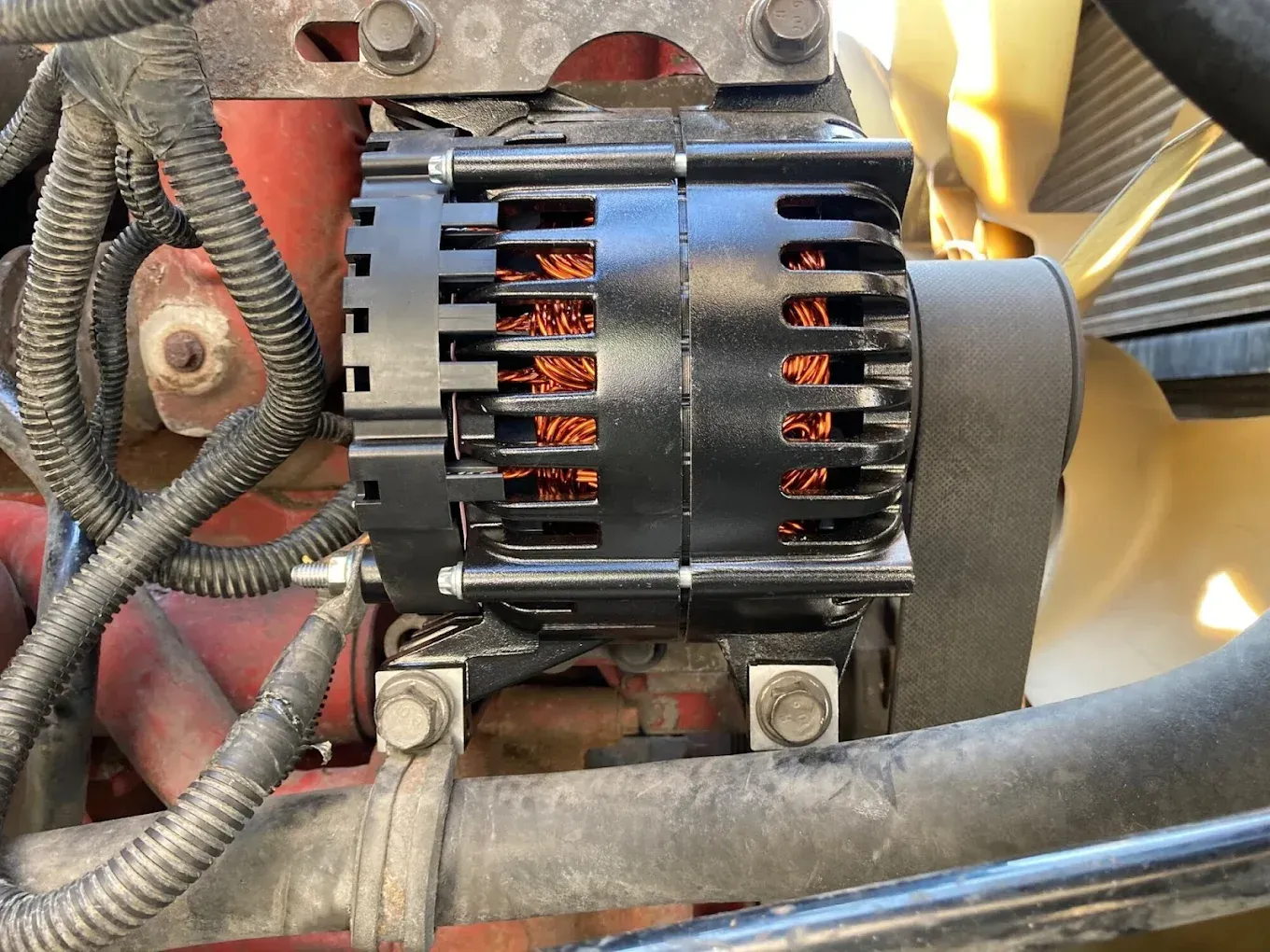 Black alternator attached to a red engine block. Wires and a fan are visible.