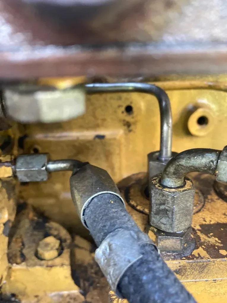 Close-up of fuel lines on a yellow engine block, showing metal tubes and rubber hose connections.