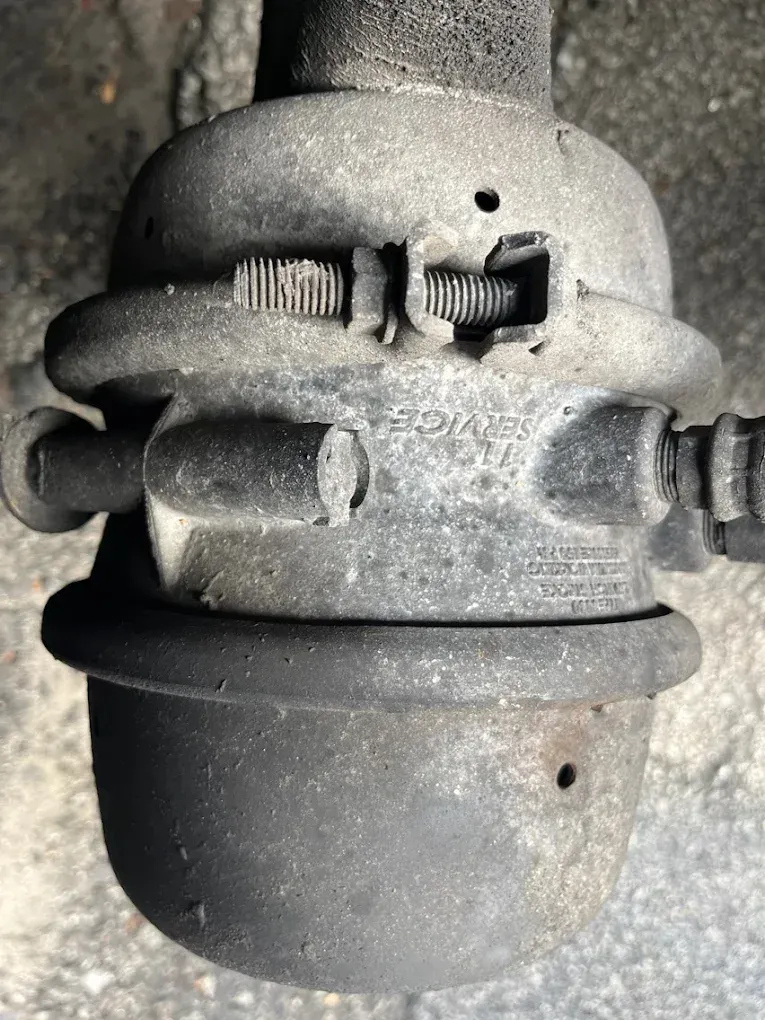 Close-up of a dusty black brake chamber with a ribbed adjustment mechanism and a small hole.