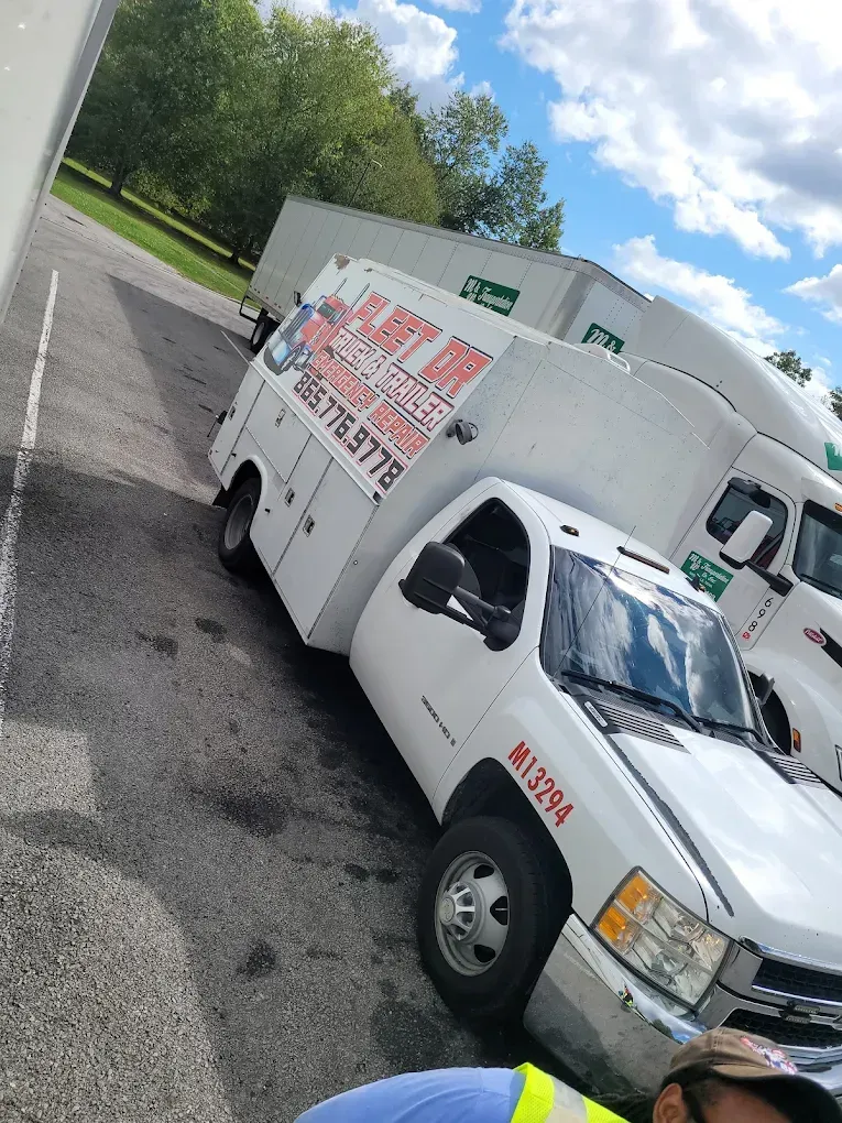 White work truck parked next to a semi-truck; text on the work truck,