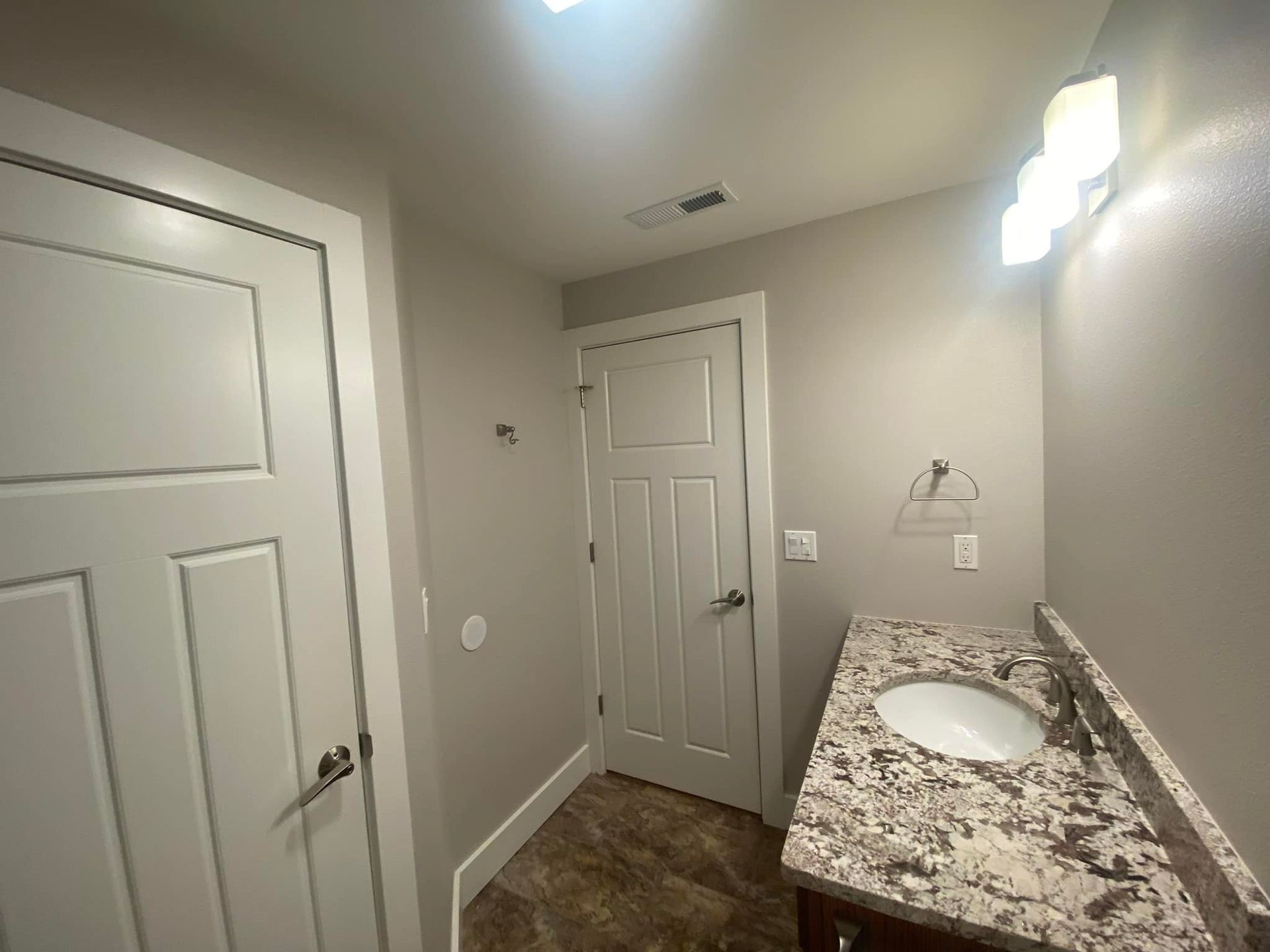 Bathroom with white door, vanity, and tan walls.