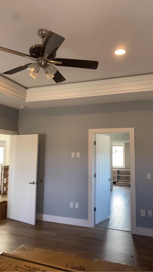 Bedroom with gray walls, white trim, two white doors, a ceiling fan, and a view into another room.