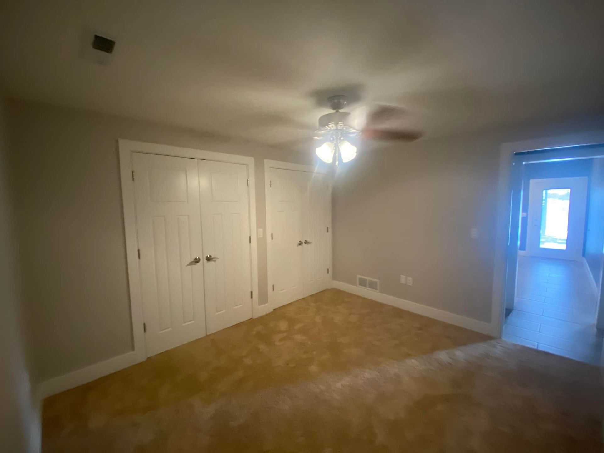 Empty bedroom with two white closet doors, tan carpet, and a door leading outside.