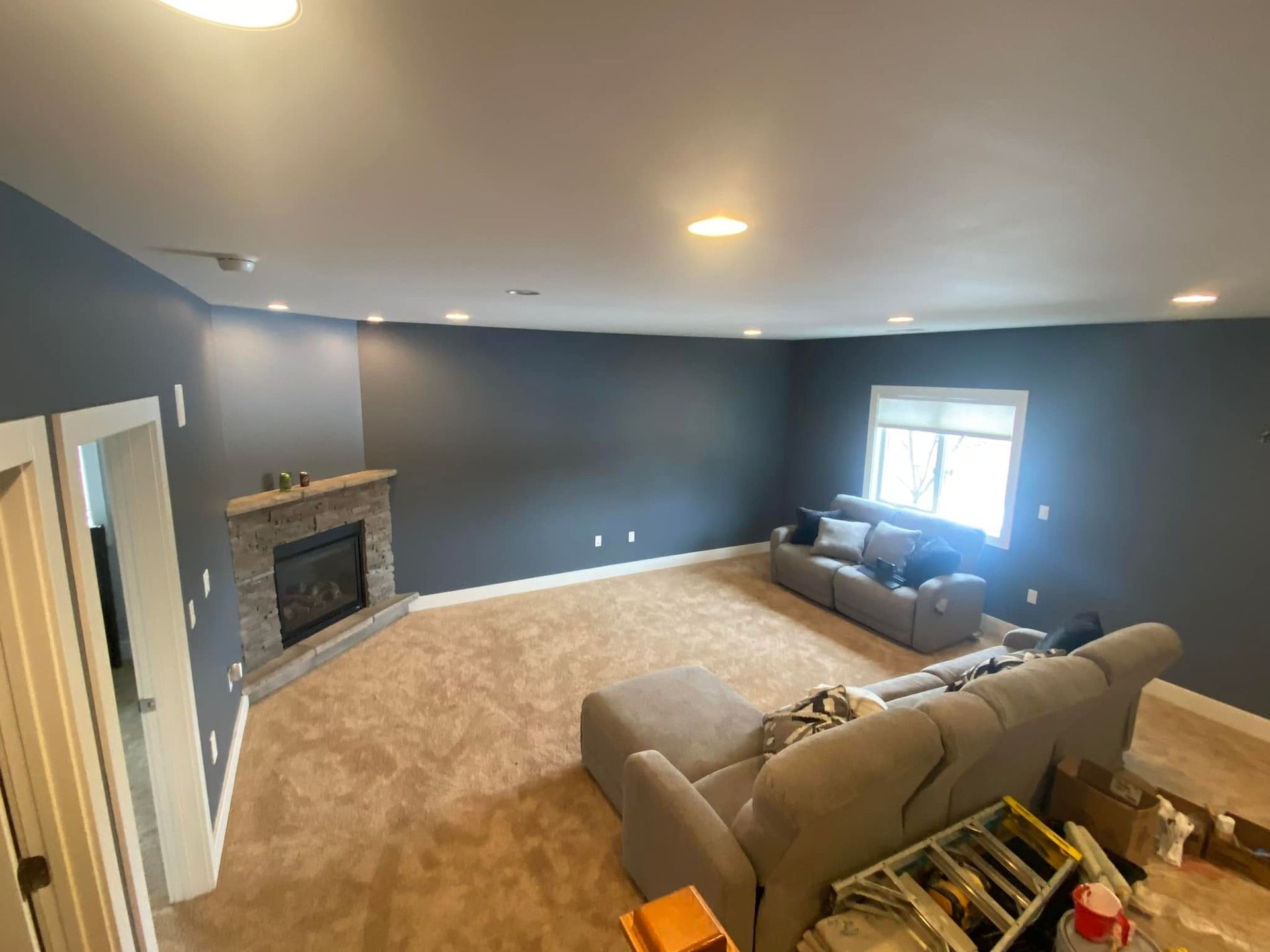 Spacious room with blue-gray walls, fireplace, and light beige carpet. Two couches face each other near a window.