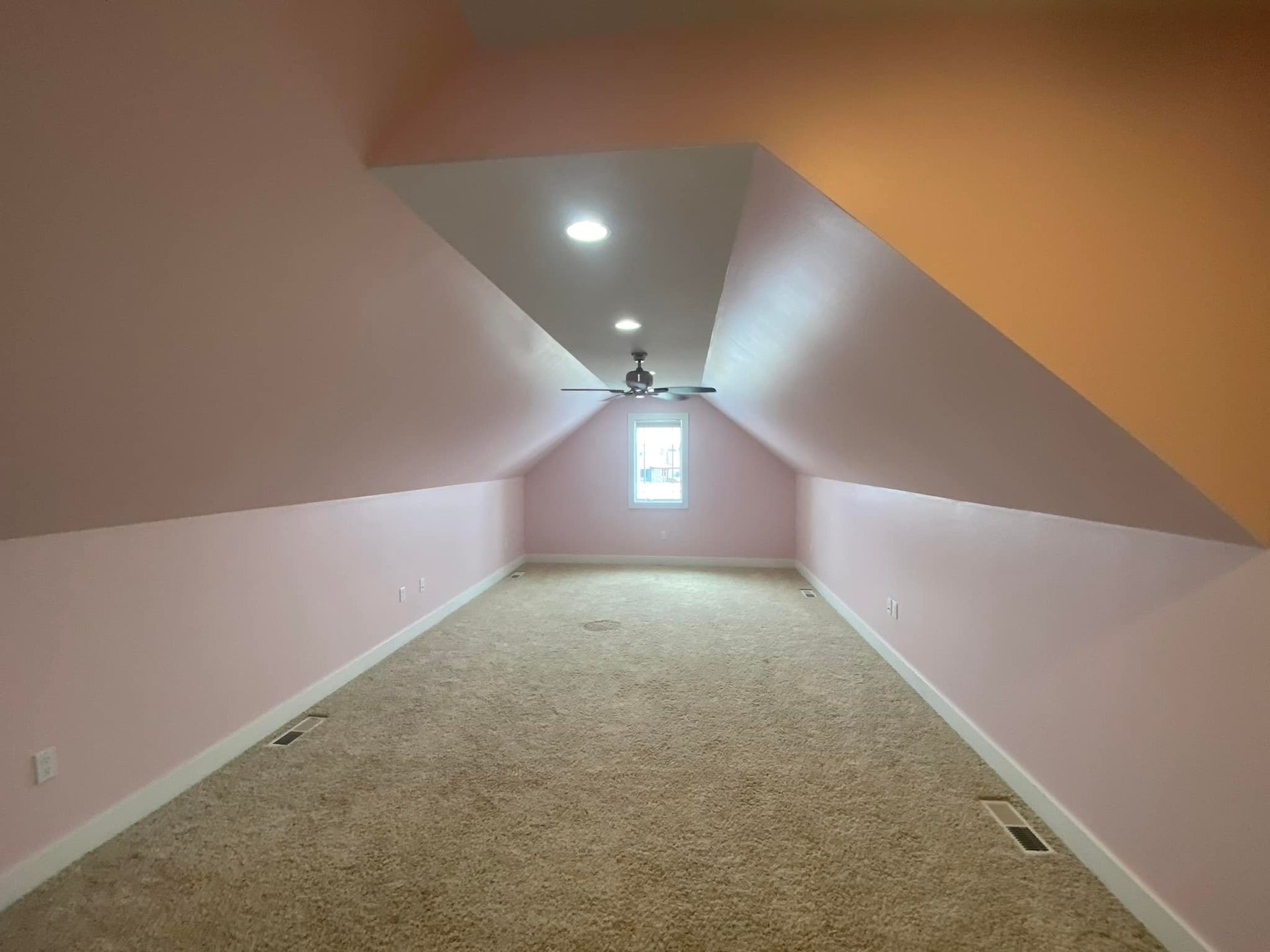 Pink and orange attic room with a tan carpet, a ceiling fan, and a small window.