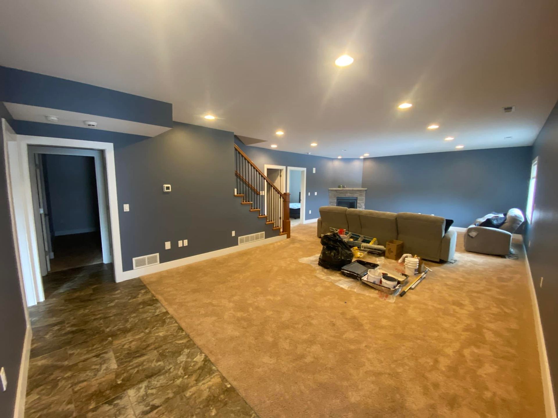 Spacious living room with gray-blue walls, tan carpet, staircase, and neutral-colored sofa.