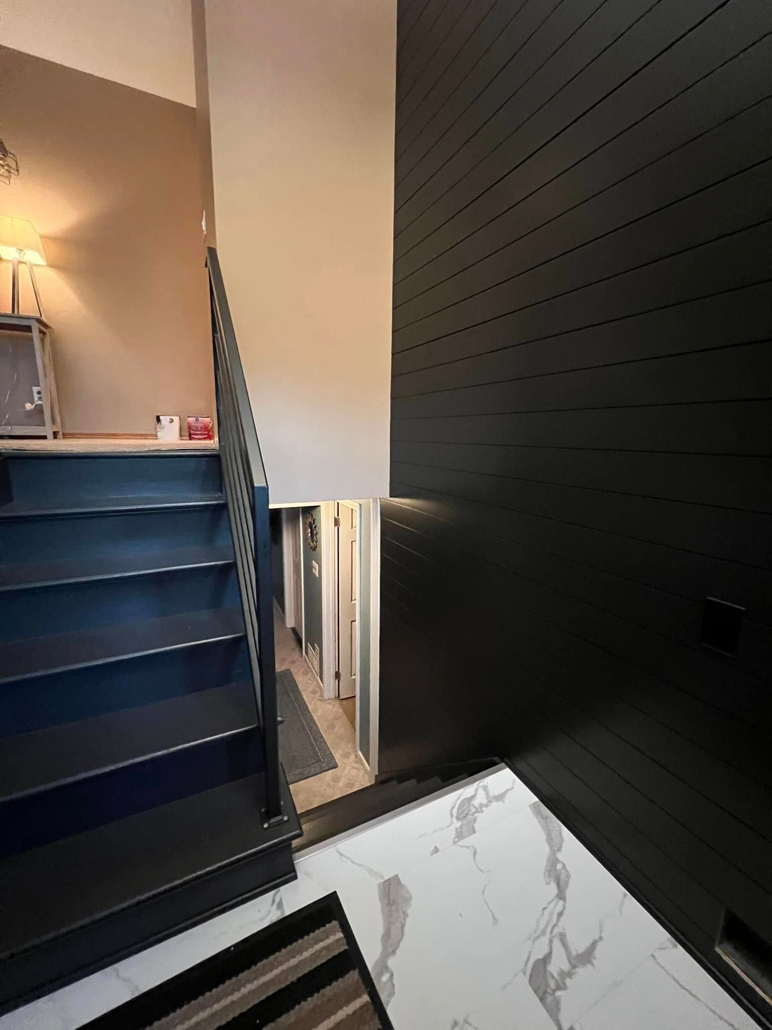 Dark staircase with black panel wall, white marbled floor and a hallway visible.