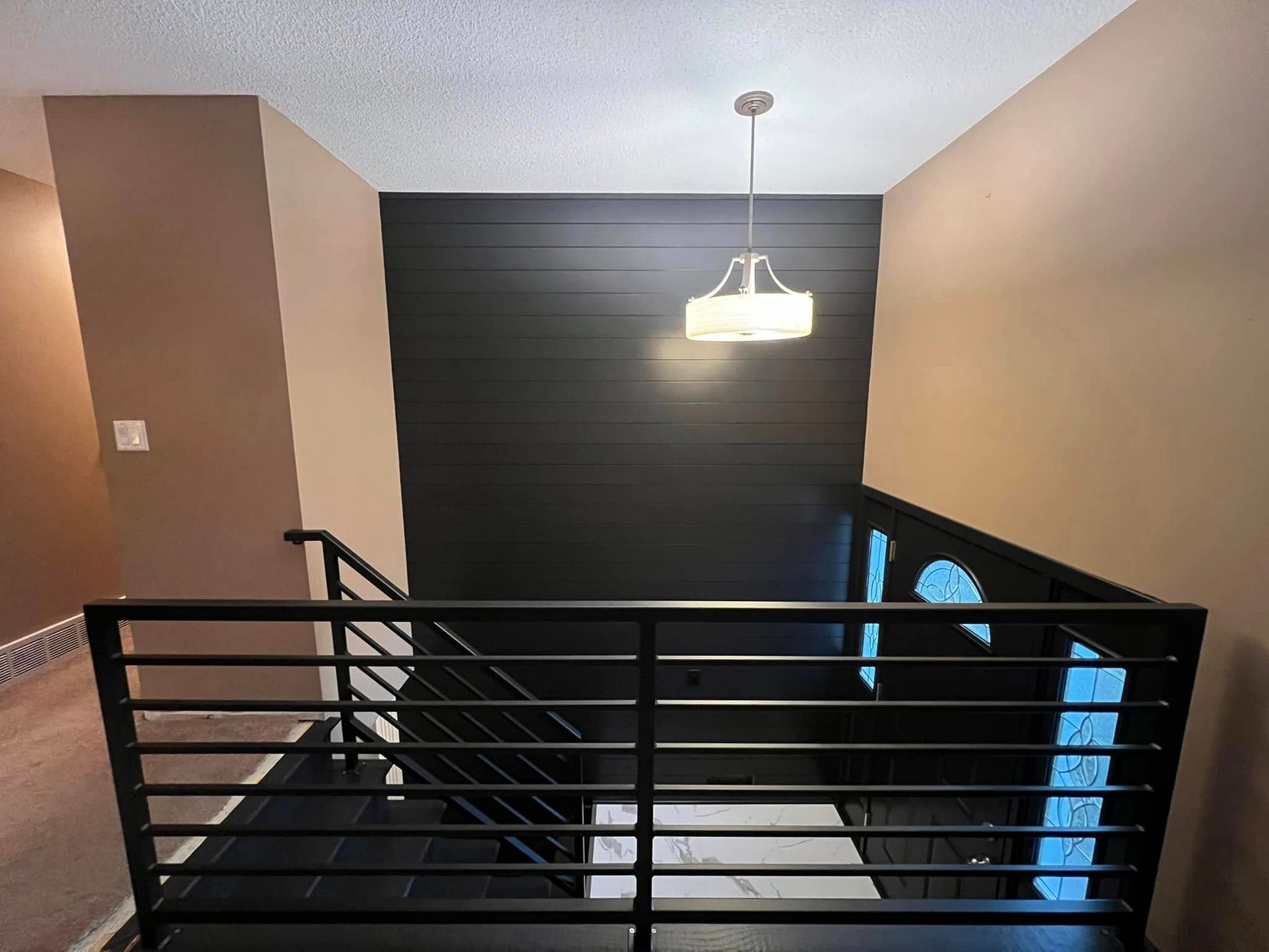 Black staircase with horizontal railing, dark accent wall, and hanging light fixture.