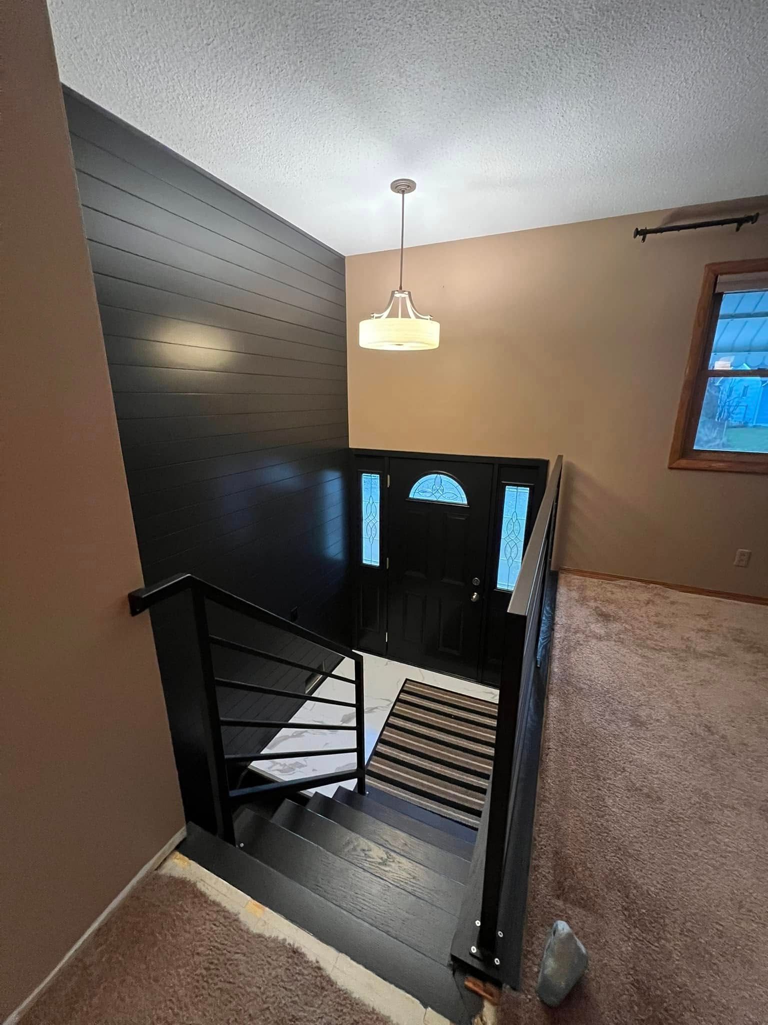 Staircase with black wall and railing, light fixture, doorway with glass, and beige carpet.