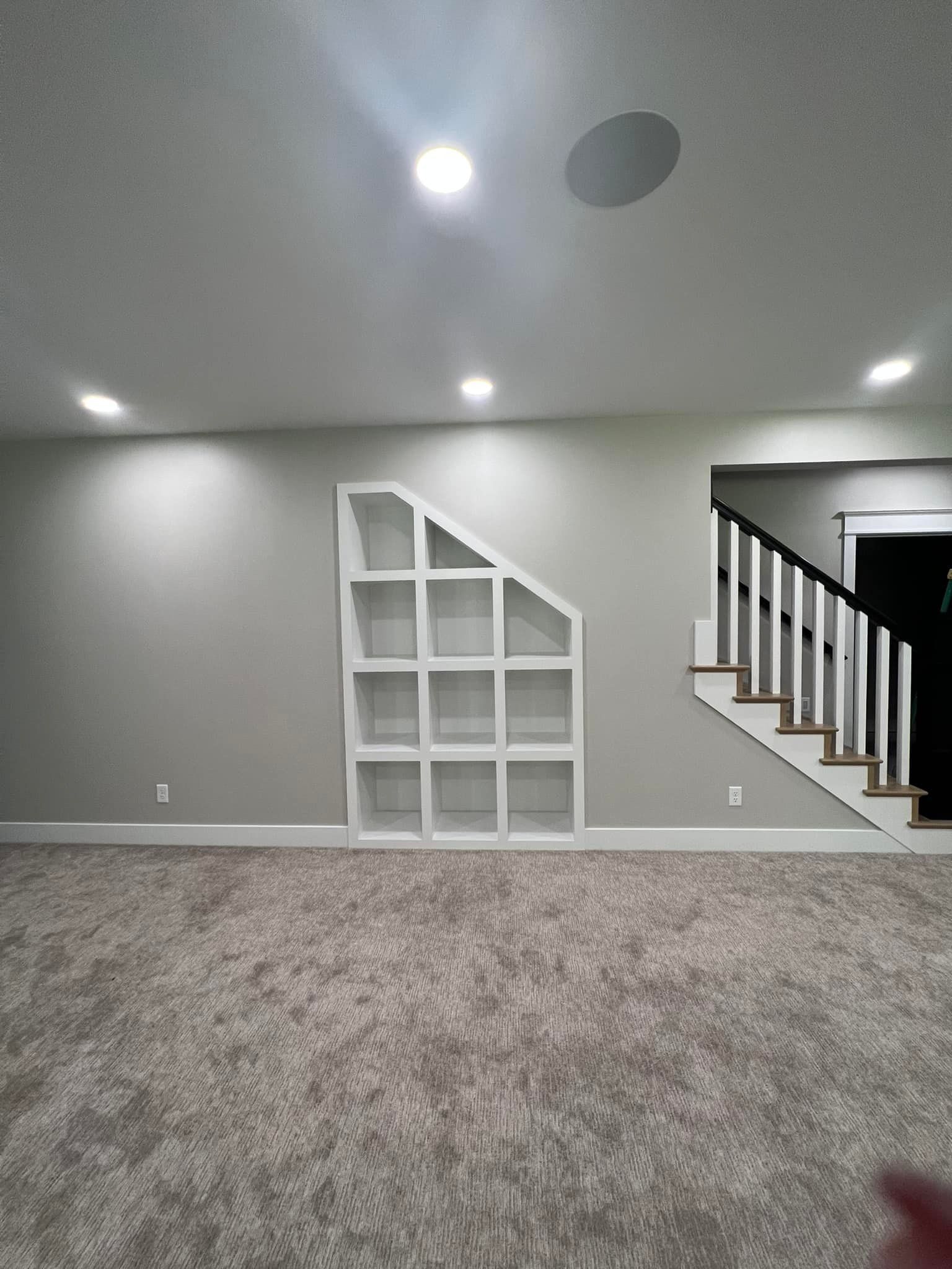Built-in white shelves in gray-painted wall. Staircase with black railing and light gray carpeted floor.