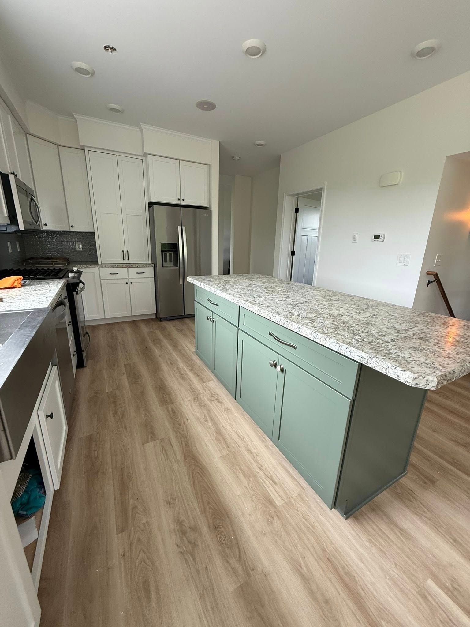 A kitchen with light wood-look flooring, white cabinets, stainless steel appliances, and a green island with a granite countertop.