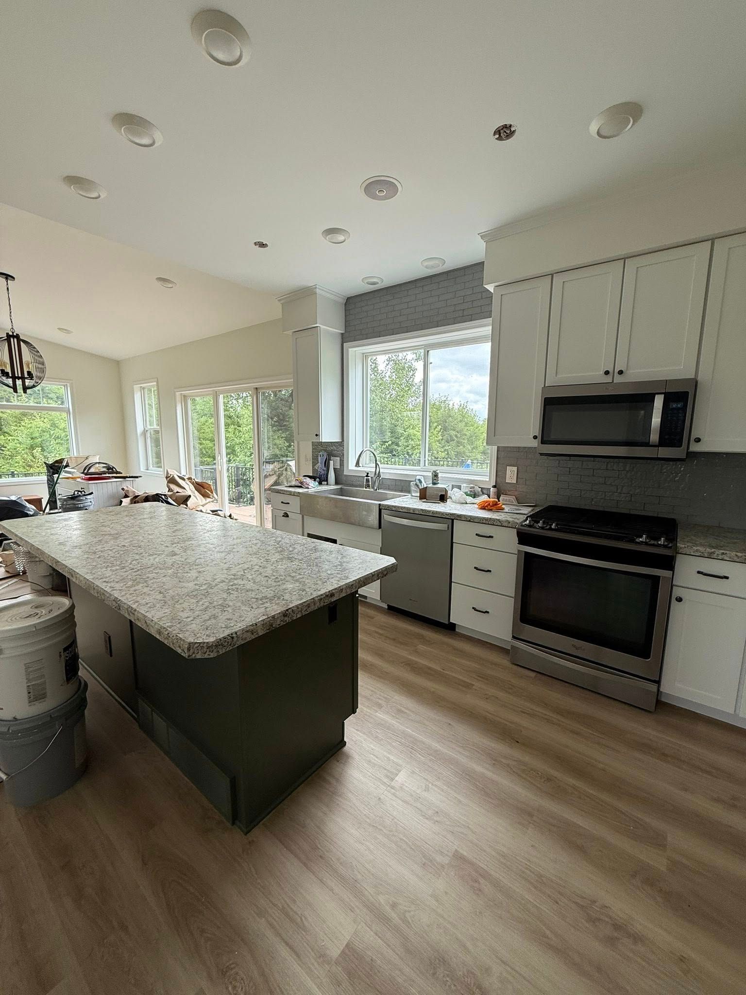 Kitchen under construction, with a green island, white cabinets, and stainless steel appliances.