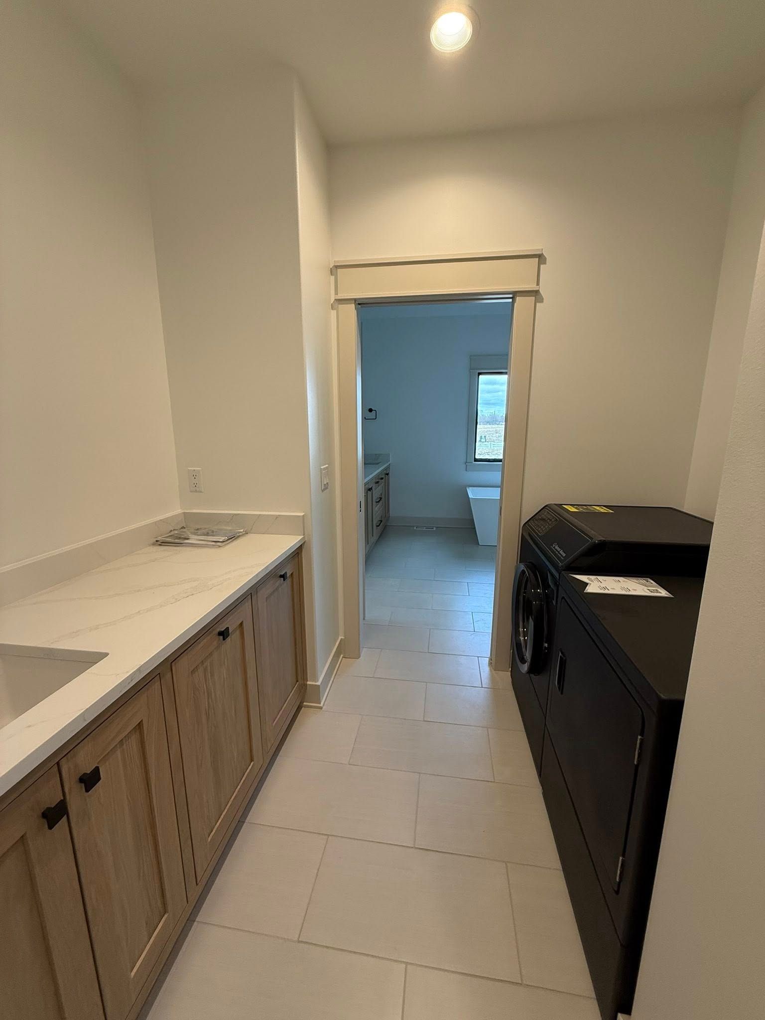 Laundry room with white counter, wood cabinets, black washer/dryer, and view into a bathroom.