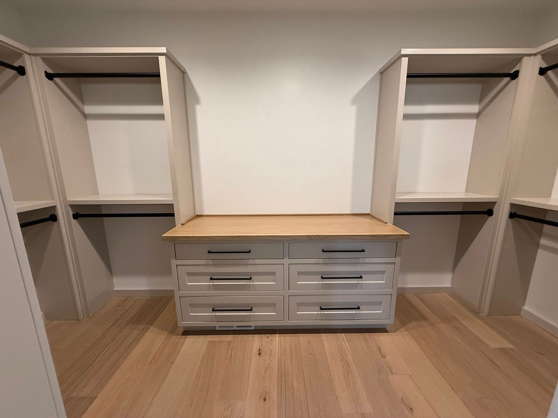 Walk-in closet with white shelves and drawers, wooden floor and countertop, and black rods.