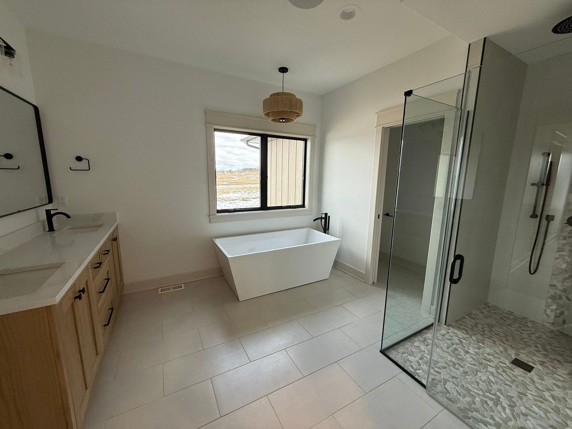 Spacious, modern bathroom with a white tub, shower, and double vanity with light wood cabinets.