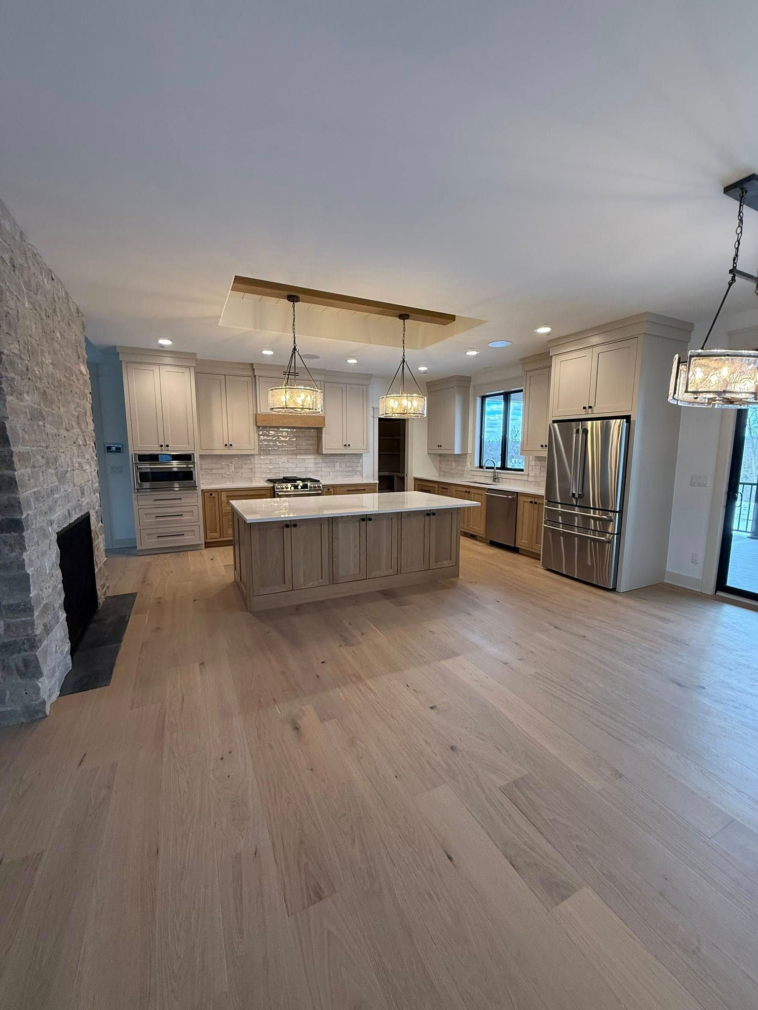 Modern kitchen with light wood cabinets, stone fireplace, and stainless steel appliances.
