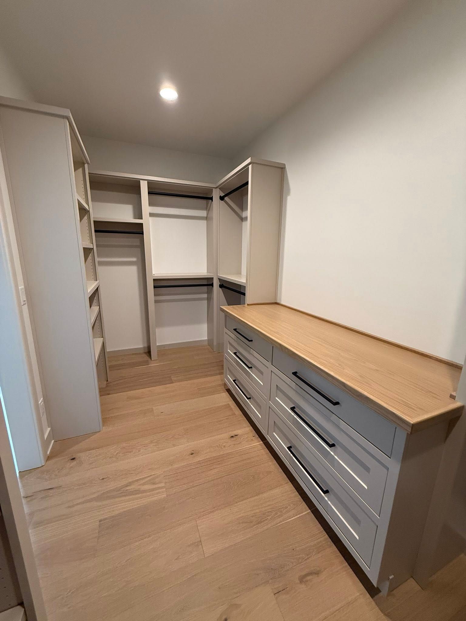 Walk-in closet with shelves and drawers. Light wood flooring and countertops, gray cabinets, white walls.