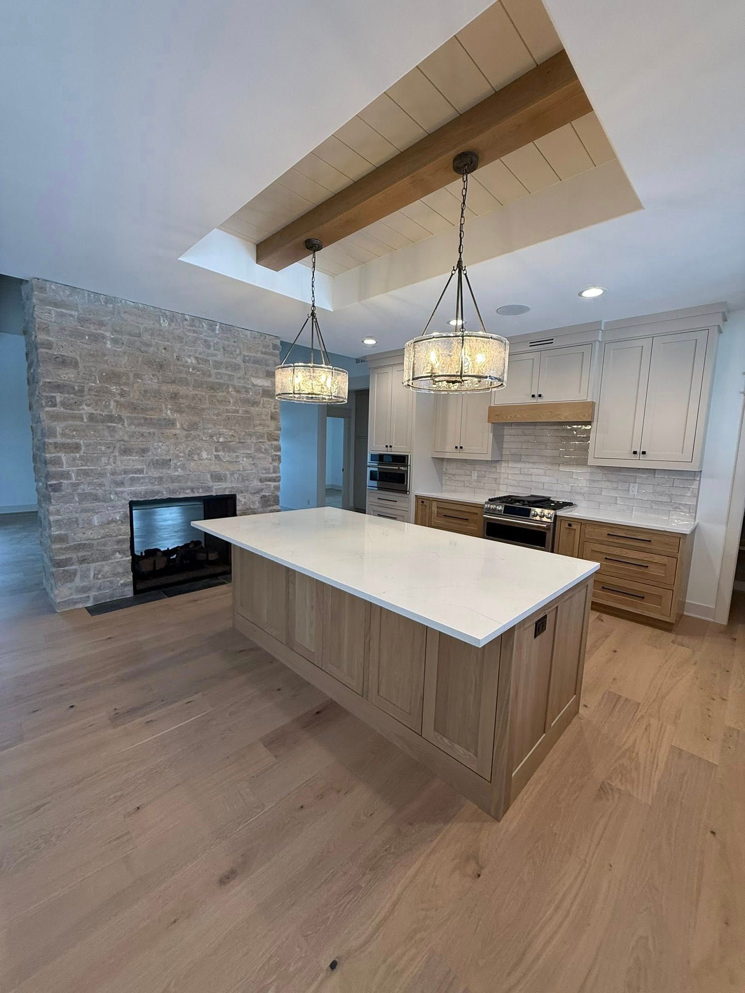 Modern kitchen with light wood island, fireplace, and pendant lights.