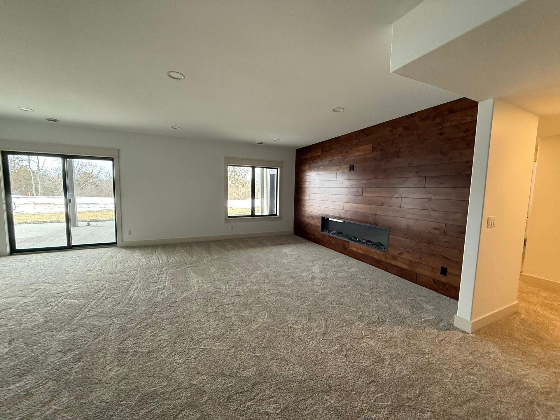 Empty room with tan carpet, a wood accent wall with a fireplace, and a sliding glass door.