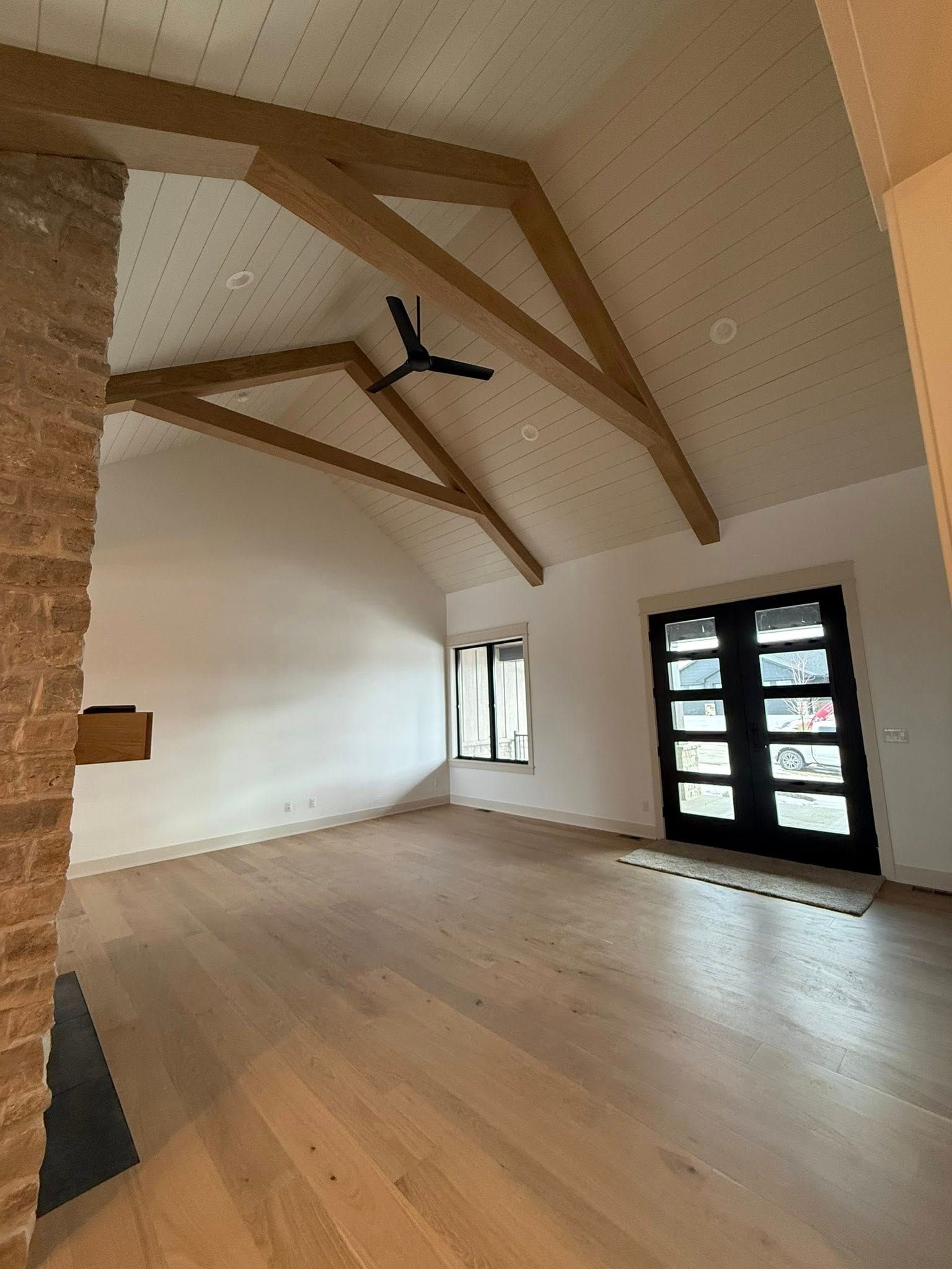 Empty living room with wood flooring, vaulted ceiling with exposed beams, and a black front door.