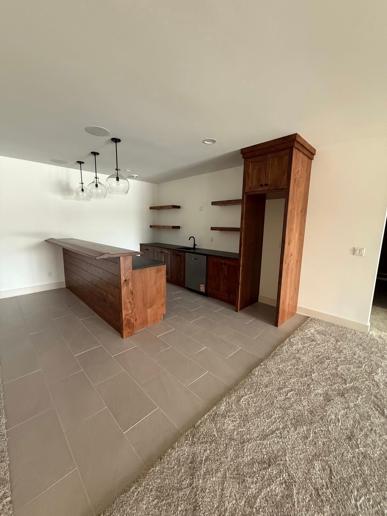 A basement bar area with a wooden bar, cabinetry, and a refrigerator space.