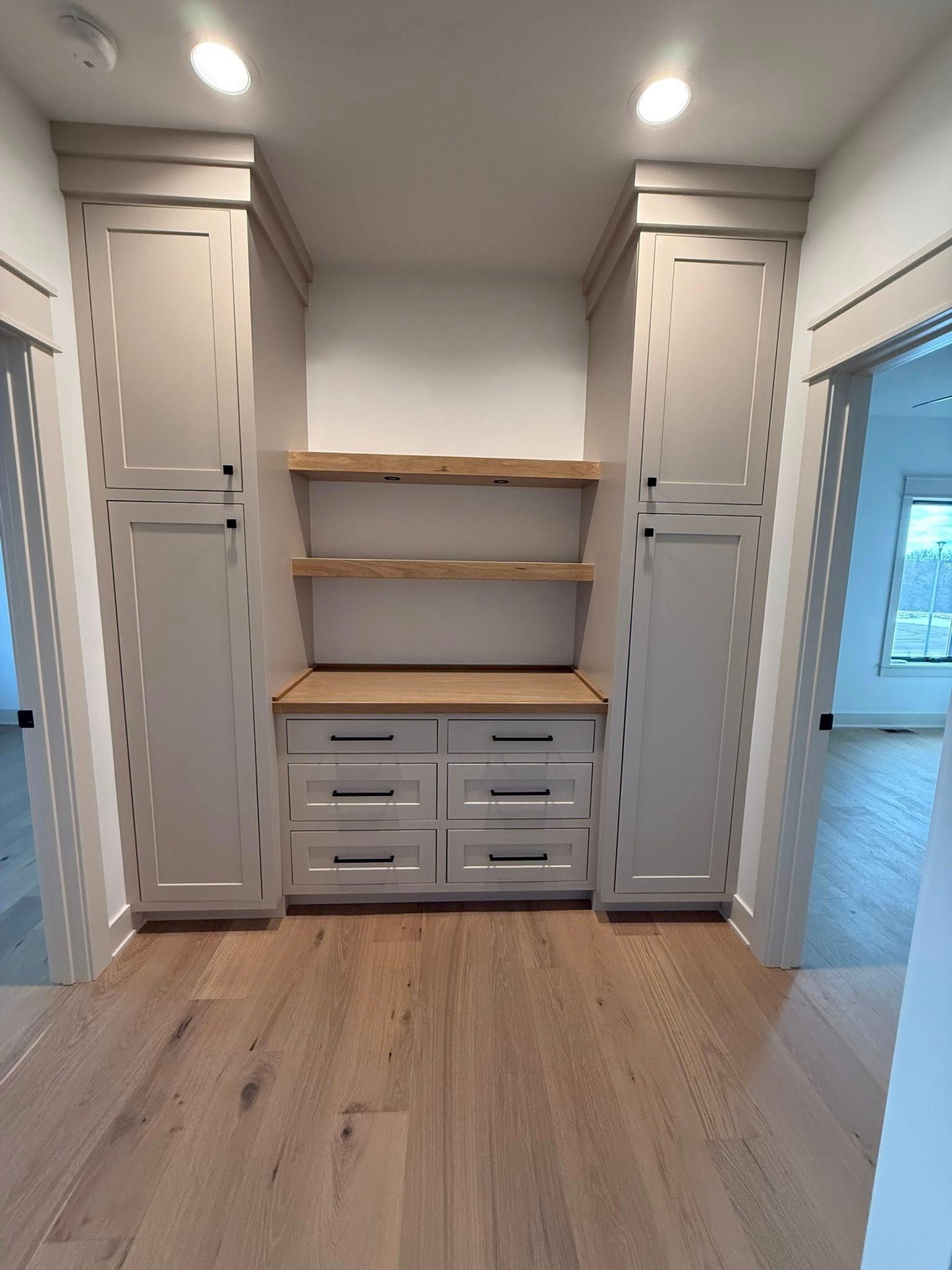 Built-in cabinetry with light-colored cabinets, wood shelves, and a drawer unit in a hallway.