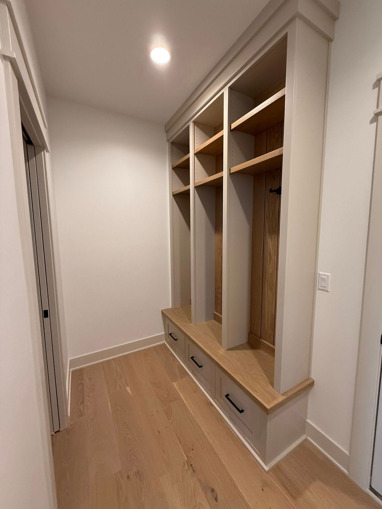 Built-in wooden entryway storage with shelves, drawers, and bench, in a hallway with wood flooring.