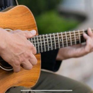 Close-up of hands playing an acoustic guitar outdoors