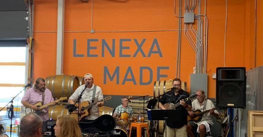 Band performing on a stage with an orange “Lenexa Made” banner in the background.