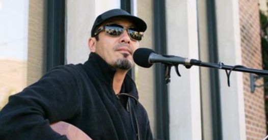Man in black cap and sunglasses speaking into a microphone outdoors