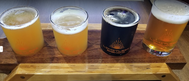 Four craft beers in glasses on a wooden tray, from pale hazy yellow to dark stout and amber lager