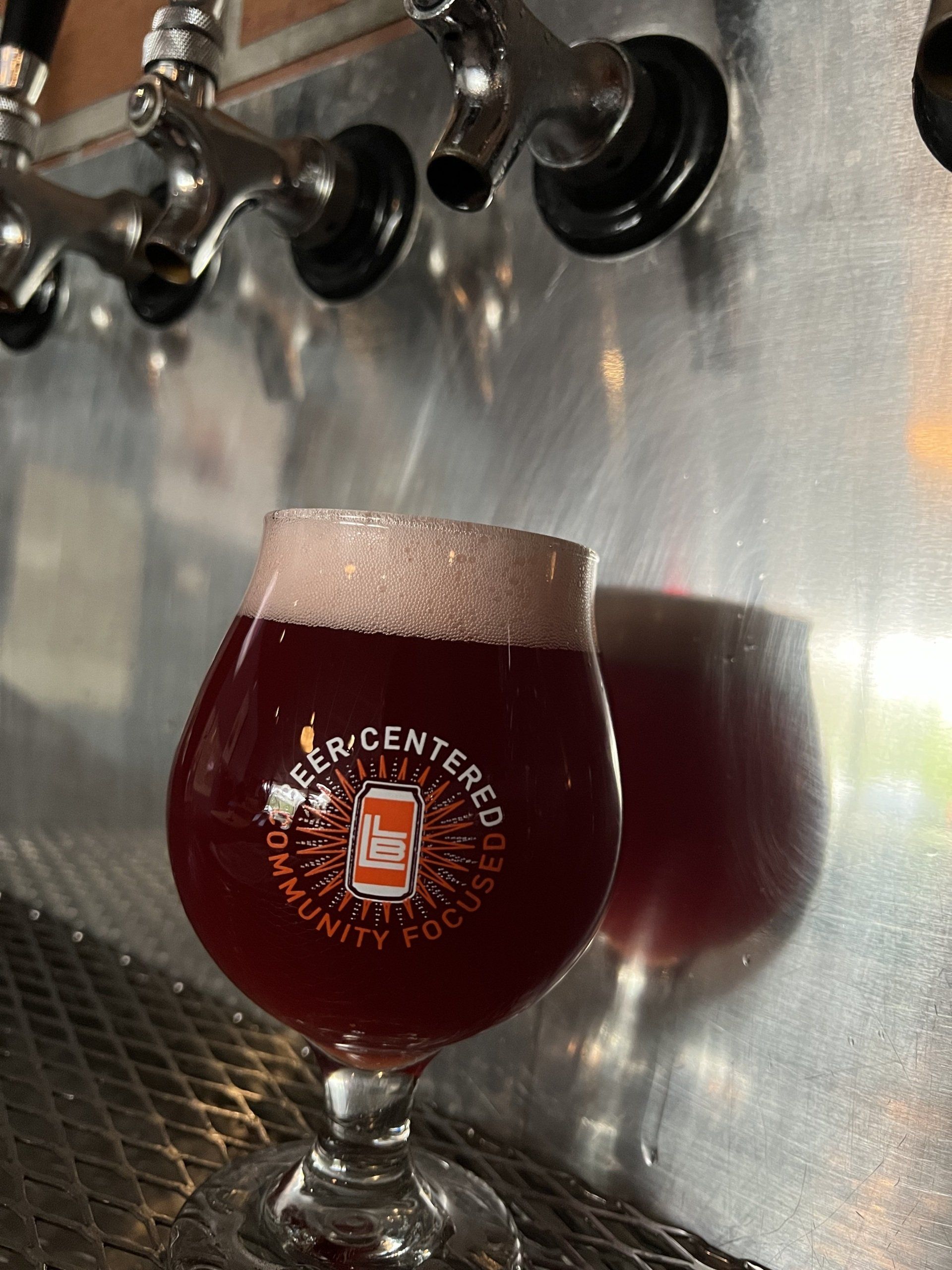 Pint of dark beer with a foamy head at a tap wall in a brewery taproom