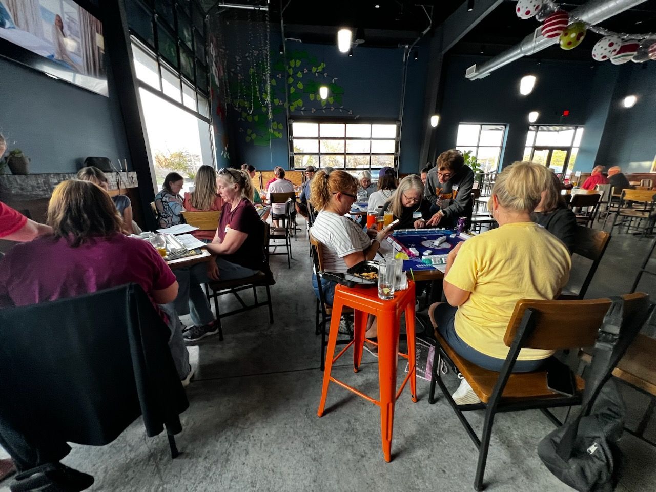 People seated at tables in a bright cafe, with orange stools and large windows.
