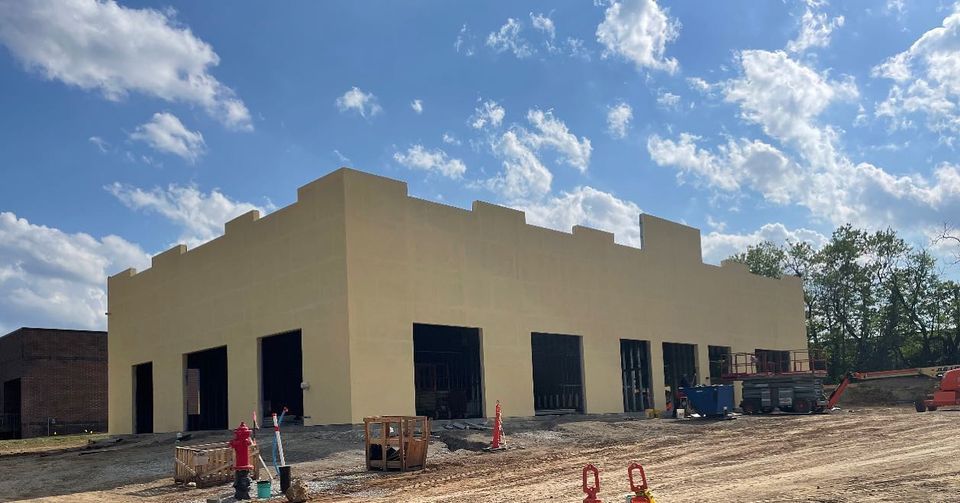 Beige building under construction with open doorways, equipment, and a blue sky with clouds.