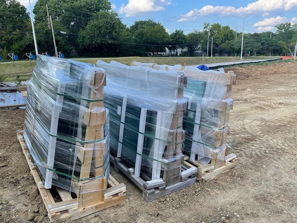 Pallets of wrapped windows and frames on a dirt lot outdoors under a cloudy sky