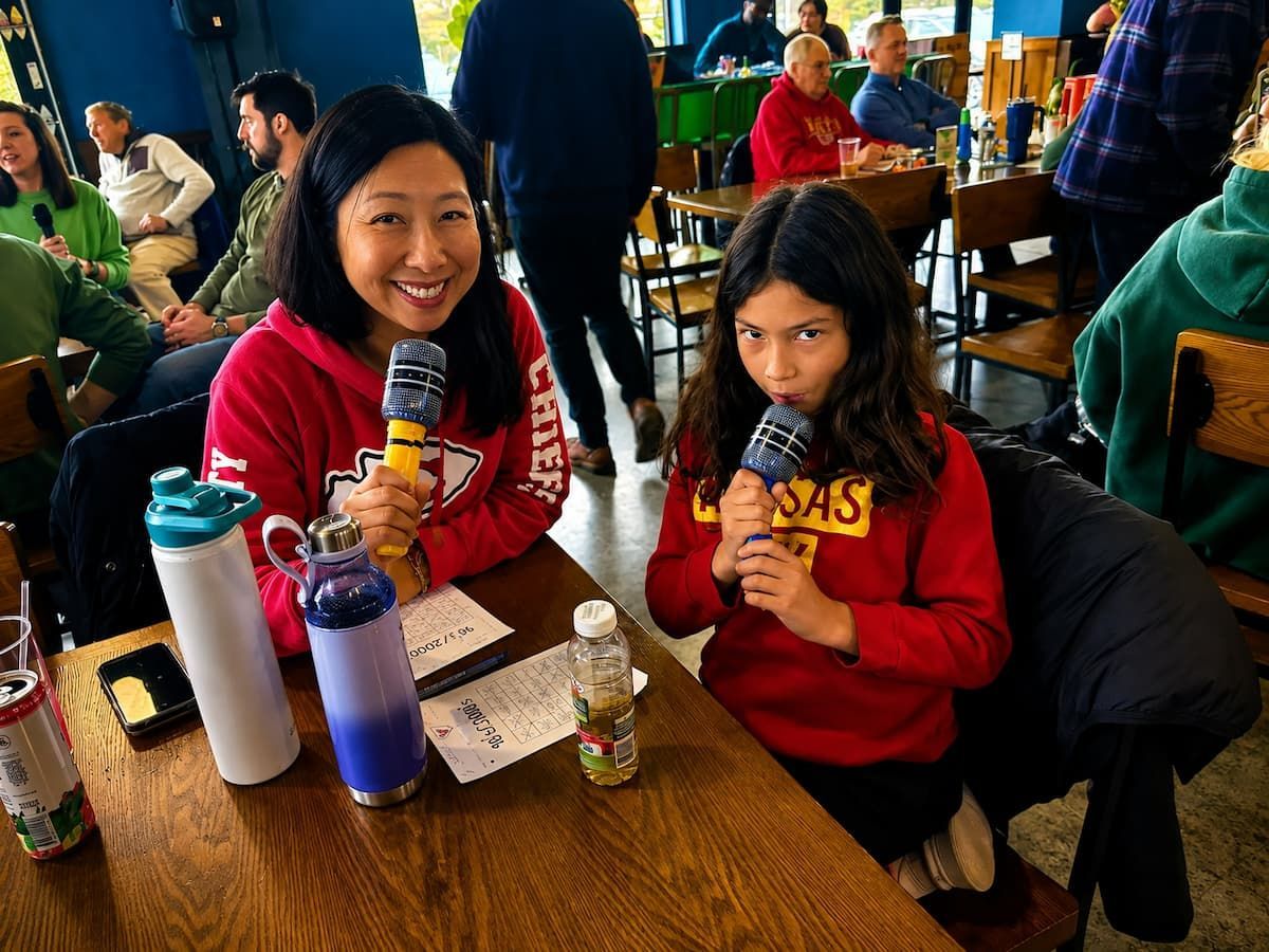 Two children in red hoodies sit at a table, smiling and holding drinks in a busy café.
