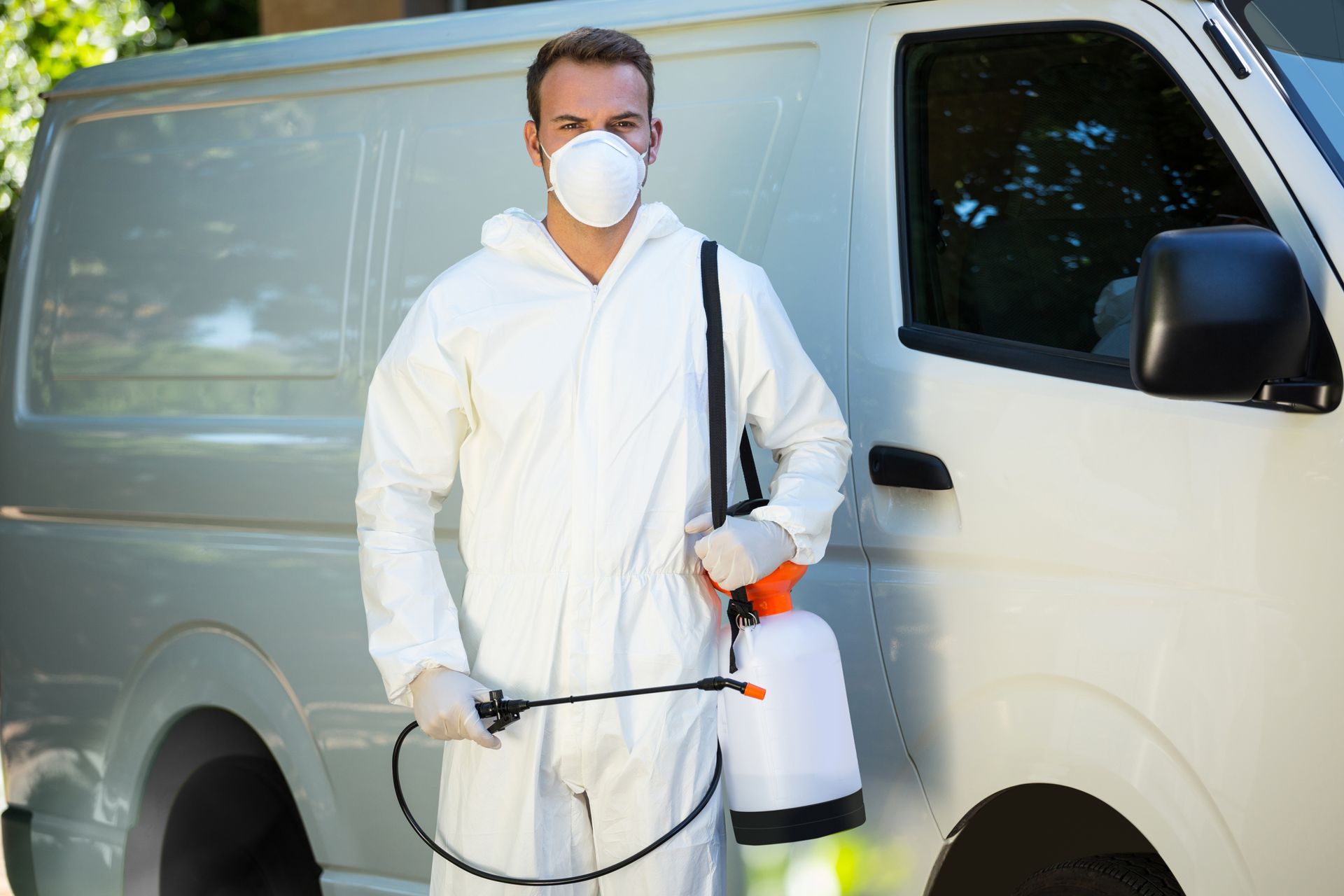 Pest control worker in protective suit with sprayer standing beside service van.